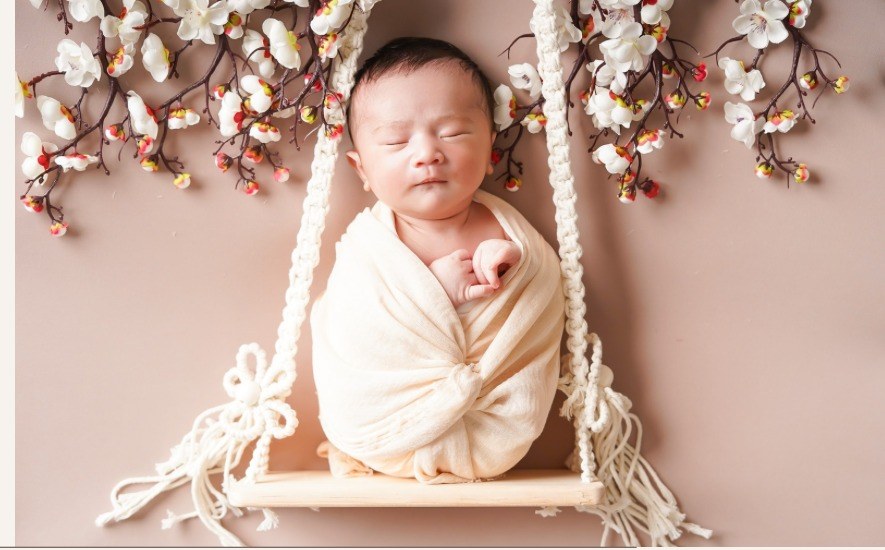 Newborn baby sleeping peacefully on a wooden swing surrounded by soft blossoms